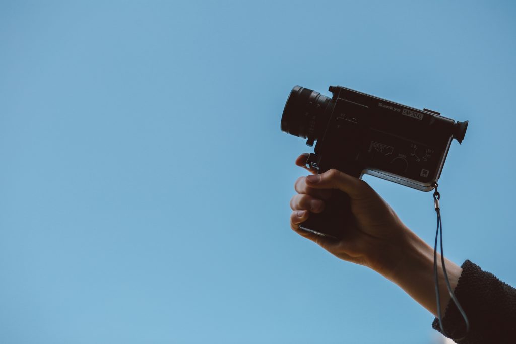 hand holding a video camera in a blue background
